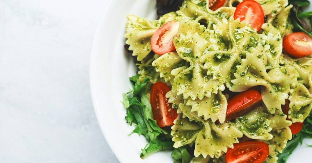 Pesto pasta with sliced tomatoes served on white ceramic plate